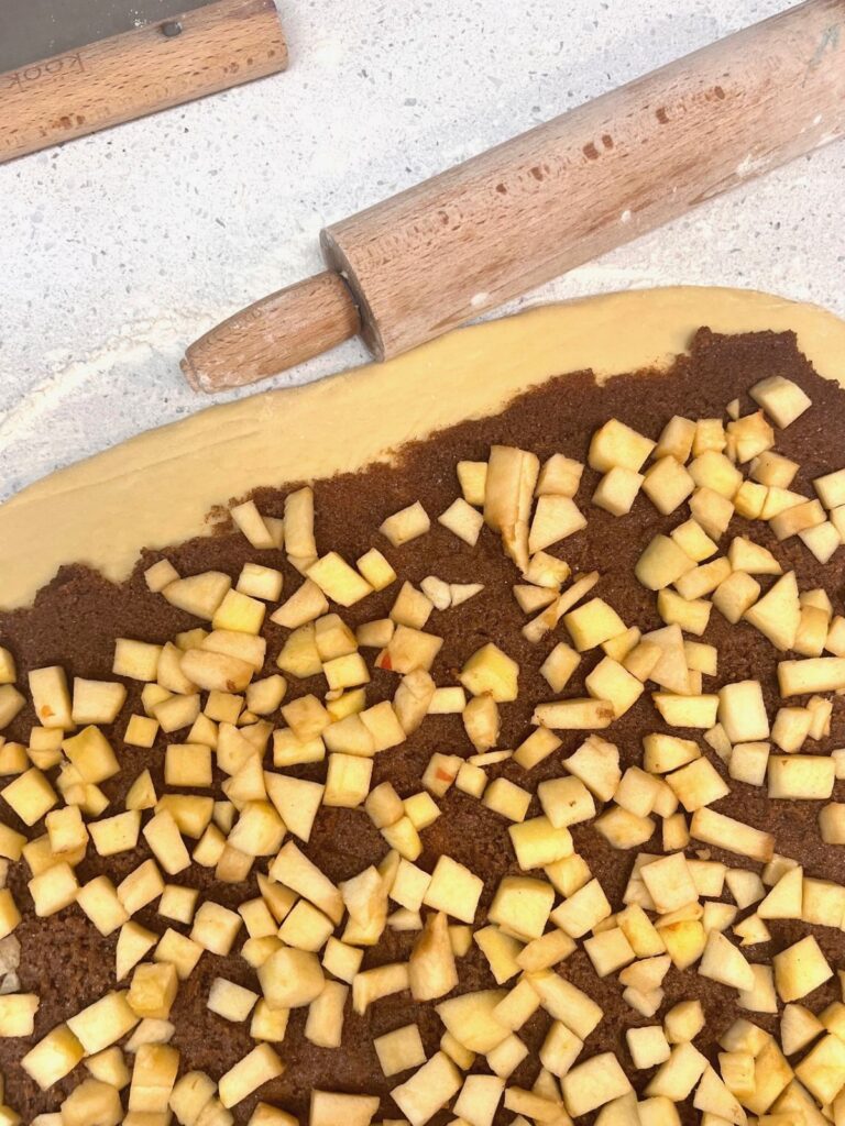 A rectangle of dough spread with cinnamon filling and sprinkled with chopped apples.
