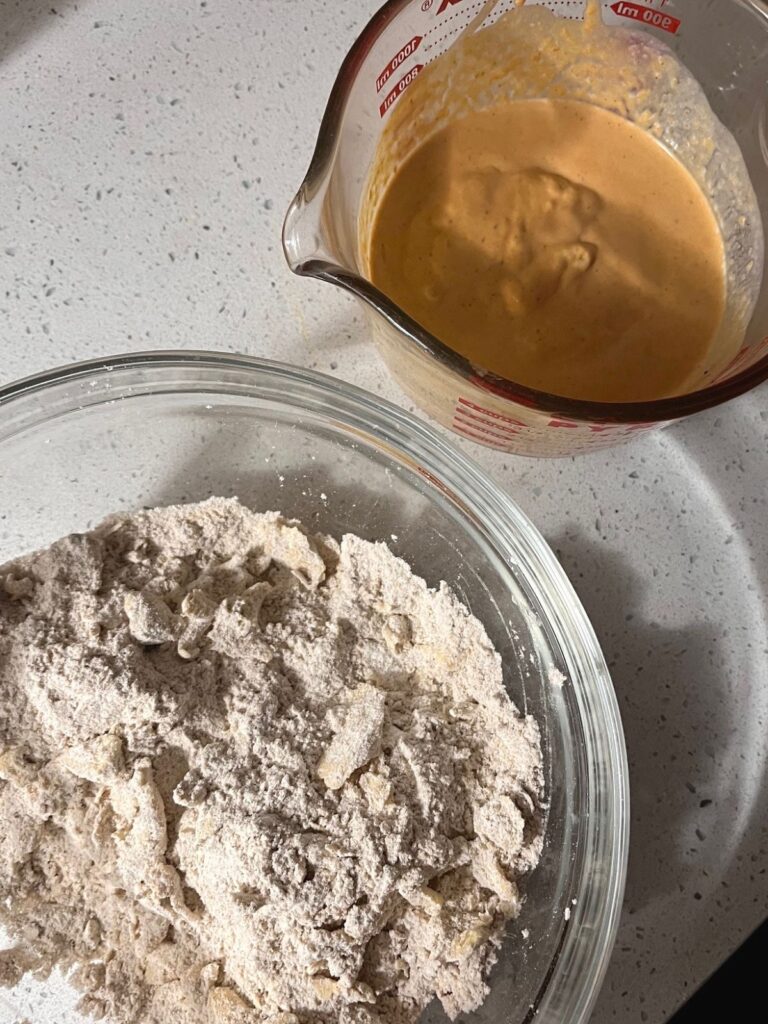 A bowl of dry ingredients and spices and a liquid measuring cup of pumpkin and sourdough and cream