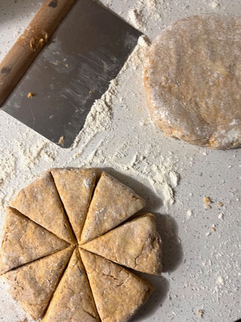 Two disks of scone dough on a floured countertop, one is sliced into 8 pieces.
