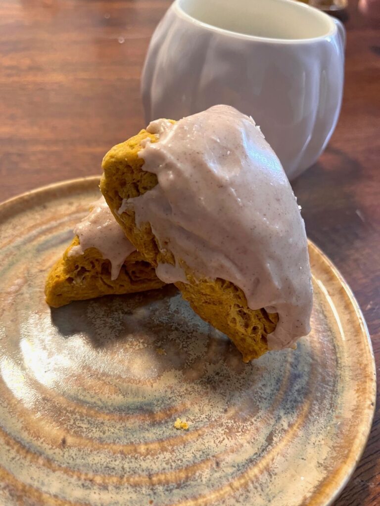 A pumpkin scone resting on another scone with a white pumpkin mug in the background.