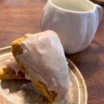 Two pumpkin sourdough scones on a brown plate with a white pumpkin mug in the background