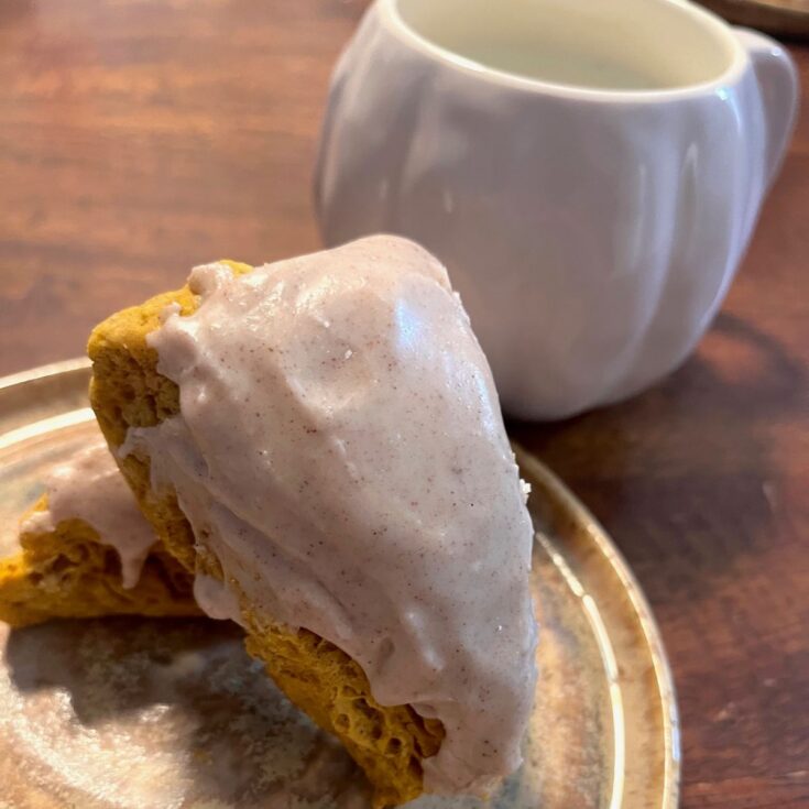 Two pumpkin sourdough scones on a brown plate with a white pumpkin mug in the background