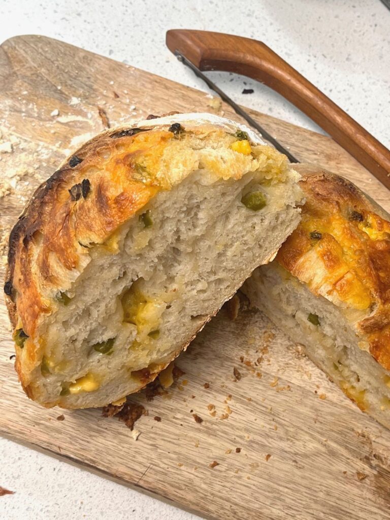 A loaf of bread cut in half and placed on a cutting board with a bow knife.