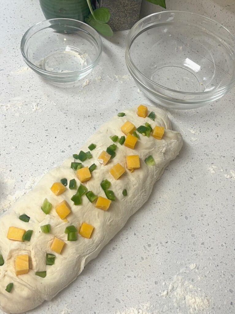 A log of bread dough with jalapeno and cheese chunks pressed into it.