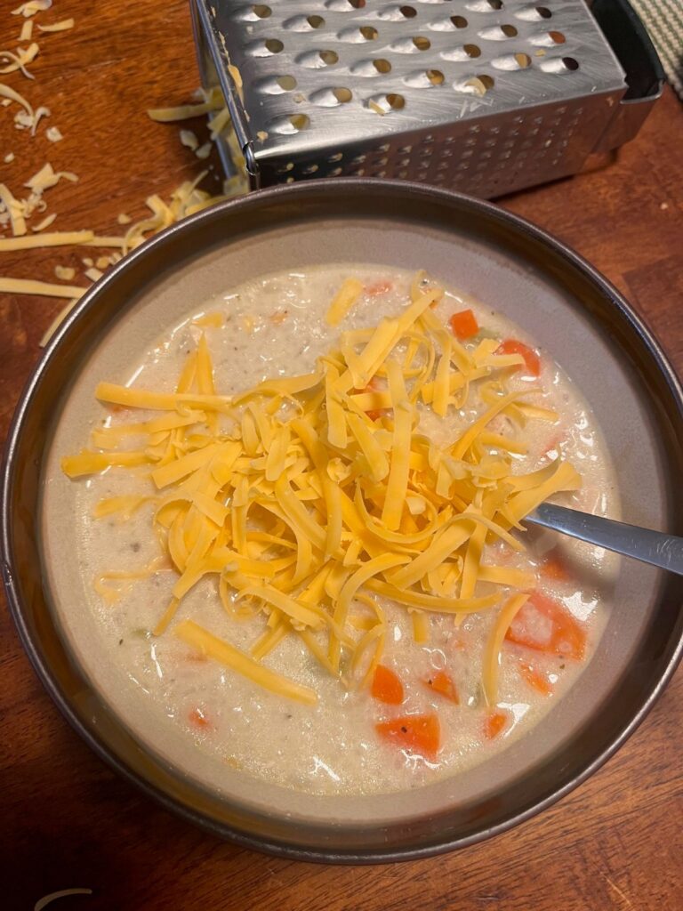A bowl of cream of chicken soup topped with grated cheddar cheese.
