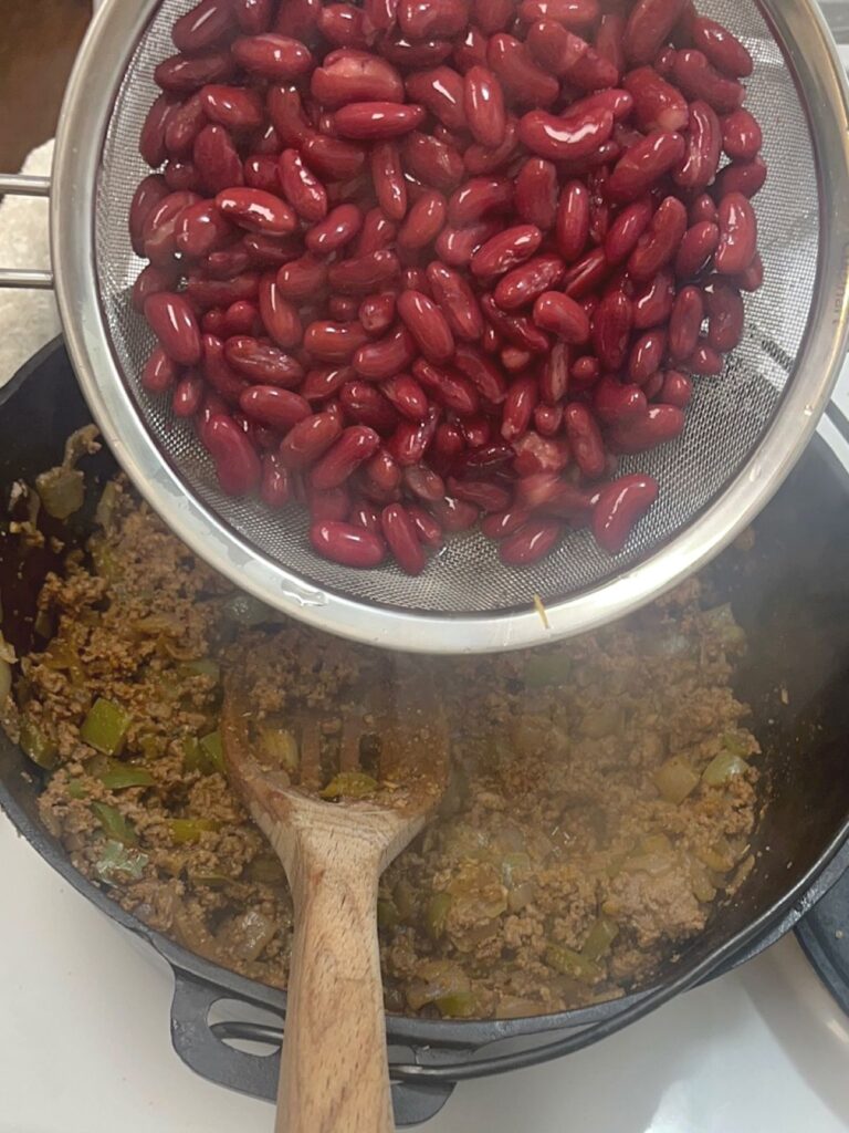 A bowl of kidney beans about to be poured into a pot with meat and peppers.