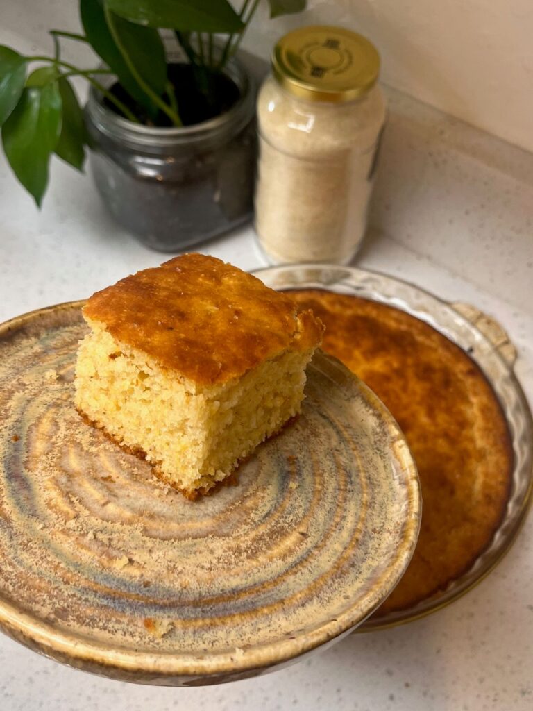 A slice of cornbread being held on a plate over a glass pie pan of cornbread.