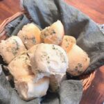 A basket filled with sourdough dinner rolls and lined with a dark green cloth napkin.
