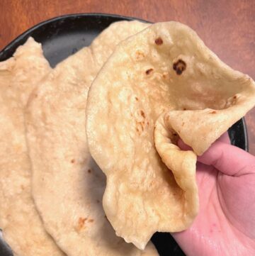 A sourdough naan bread being folded and pinched over a plate of more naan breads.