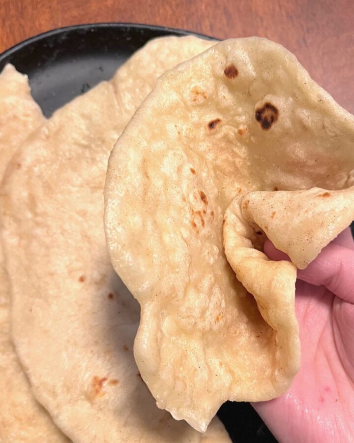 A sourdough naan bread being folded and pinched over a plate of more naan breads.