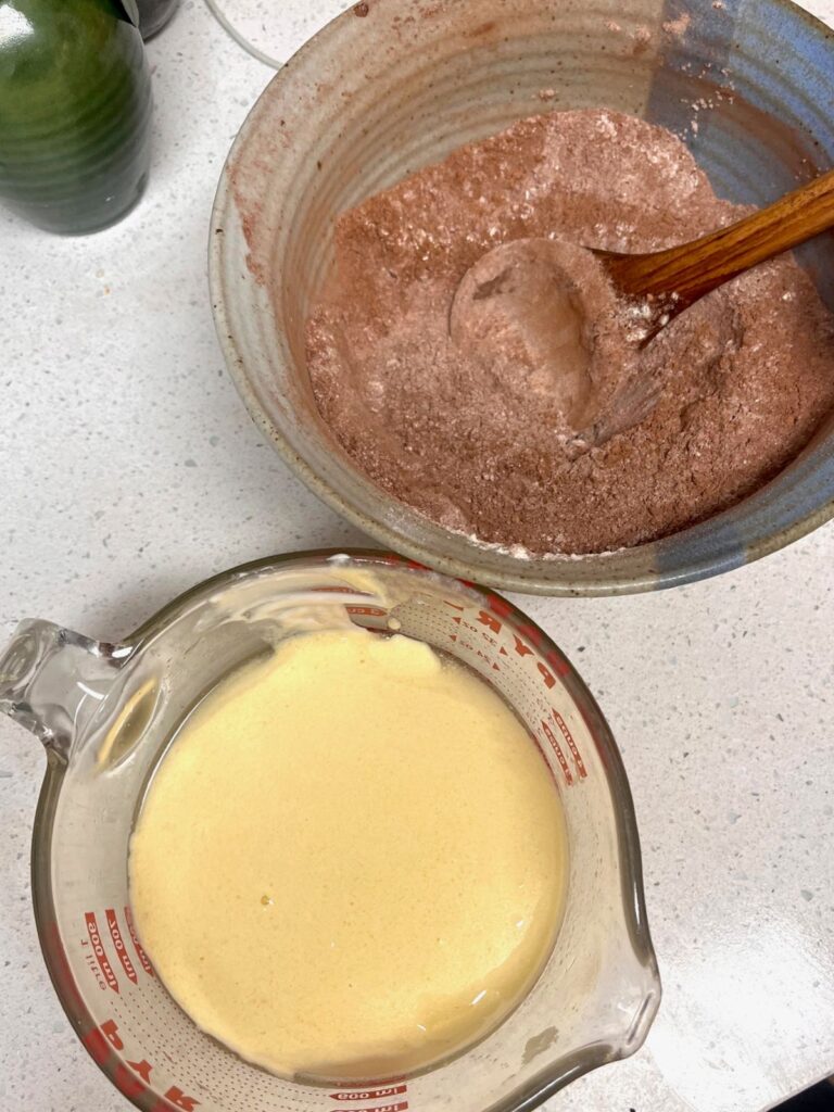A large liquid measuring cup next to a bowl with cocoa and other dry ingredients.
