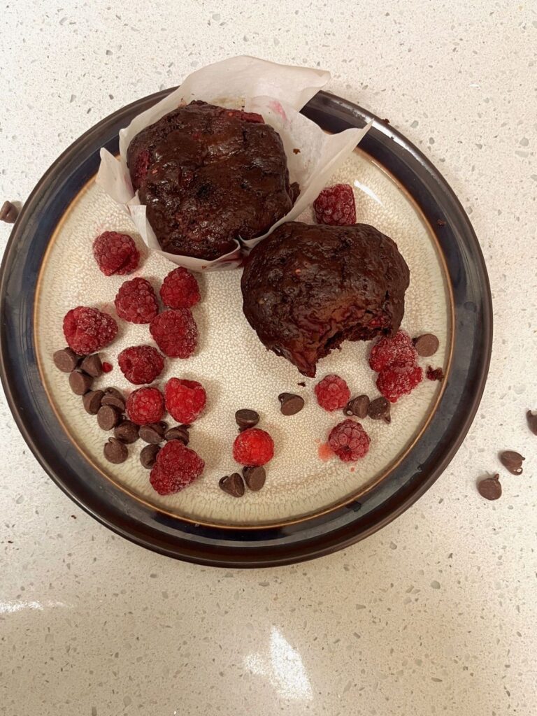 A plate with a muffin, chocolate chips, and raspberries. 