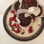 A pile of chocolate raspberry sourdough muffins on a plate with red raspberries and chocolate chips.