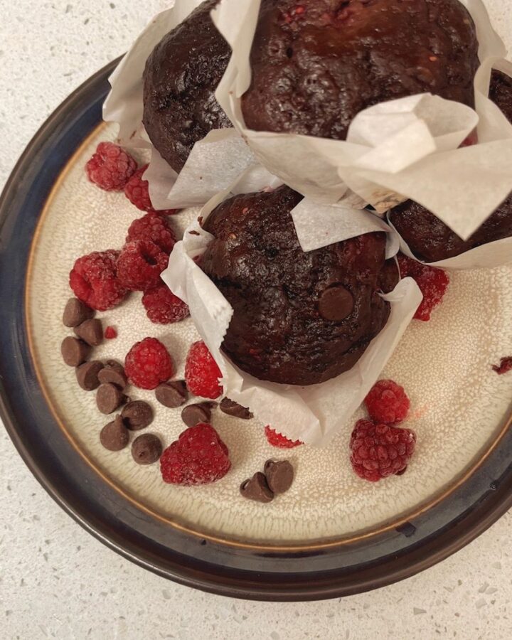 A pile of chocolate raspberry sourdough muffins on a plate with red raspberries and chocolate chips.