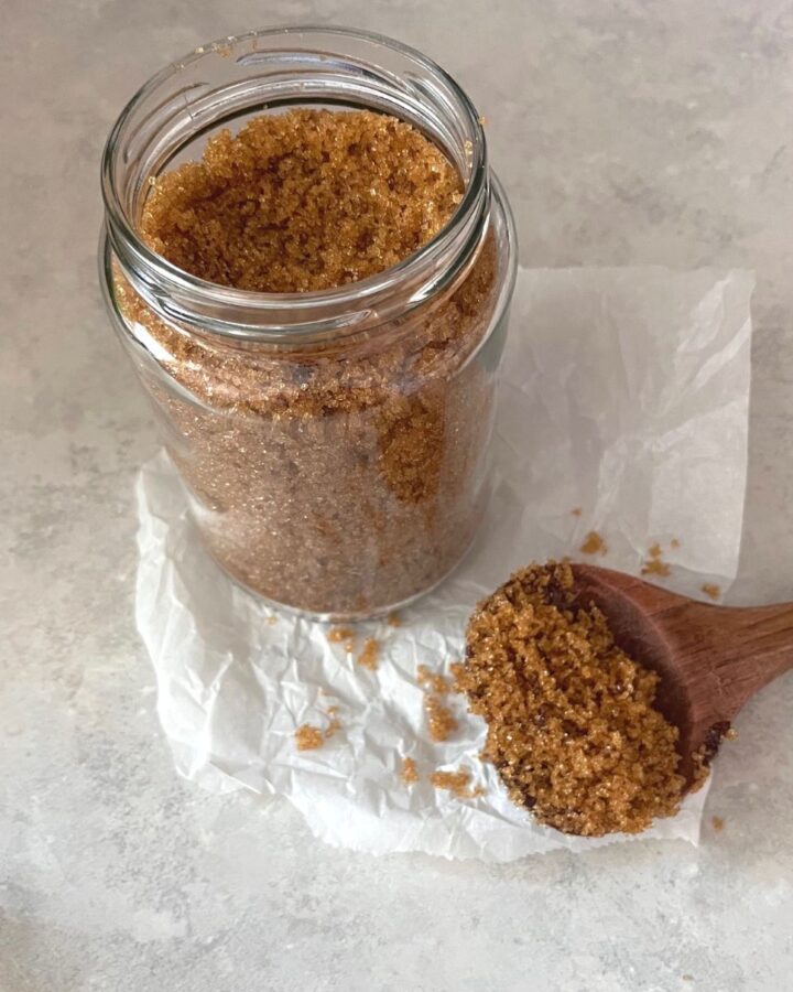 A jar of Homemade brown sugar with a wooden spoon of it resting on a piece of parchment paper.