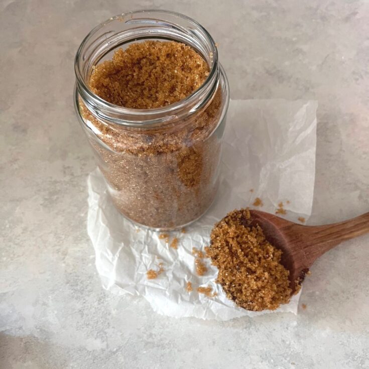 A jar of Homemade brown sugar with a wooden spoon of it resting on a piece of parchment paper.